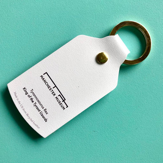 The back of the white leather keyring with museum branding in black. Placed on a turquoise background.