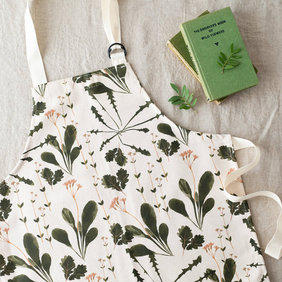 Load image into Gallery viewer, Lifestyle shot showing half of the apron on a grey background with a green book in the top right corner.
