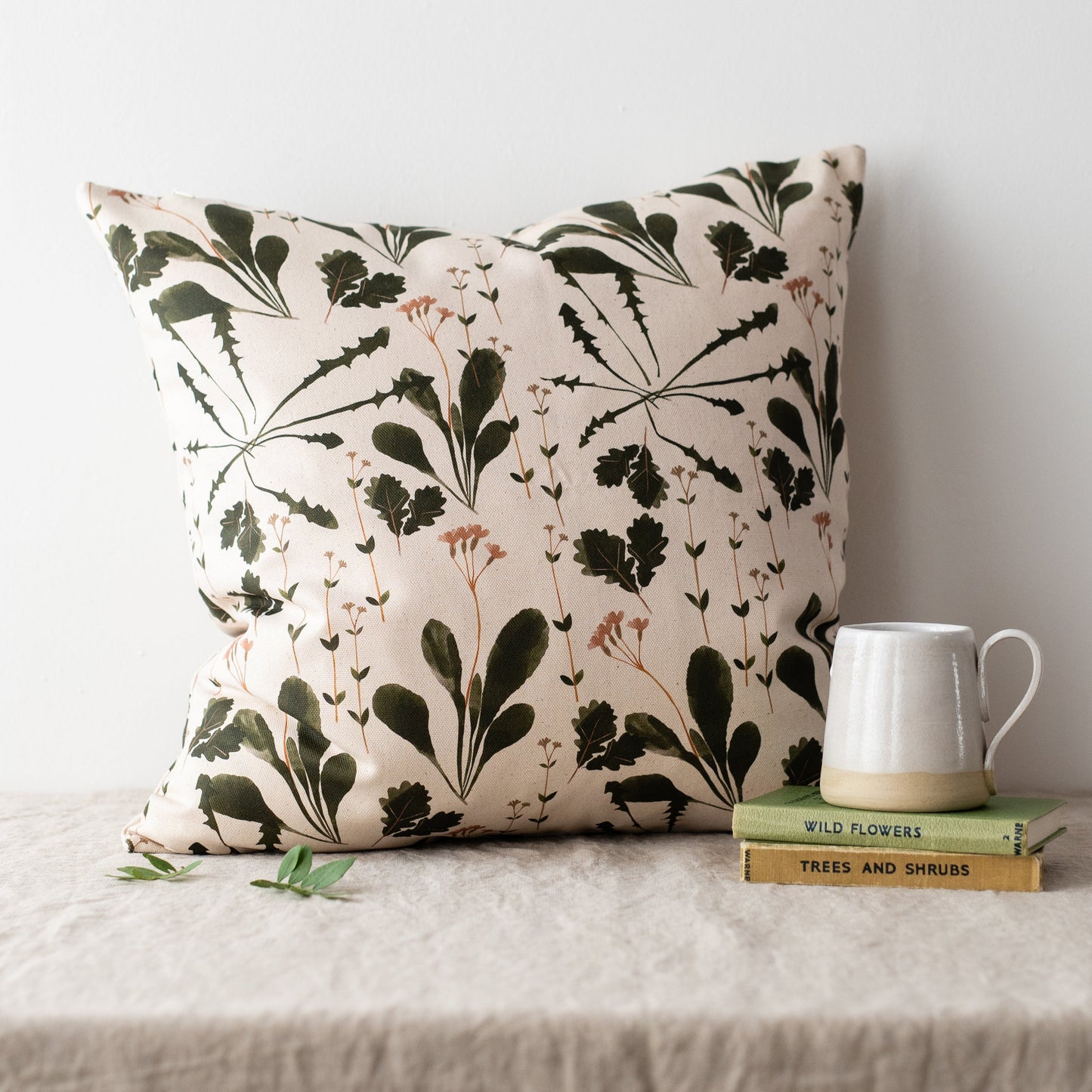 Load image into Gallery viewer, Lifestyle shot of a stuffed pillow on a grey surface with two green books and a mug on the right.
