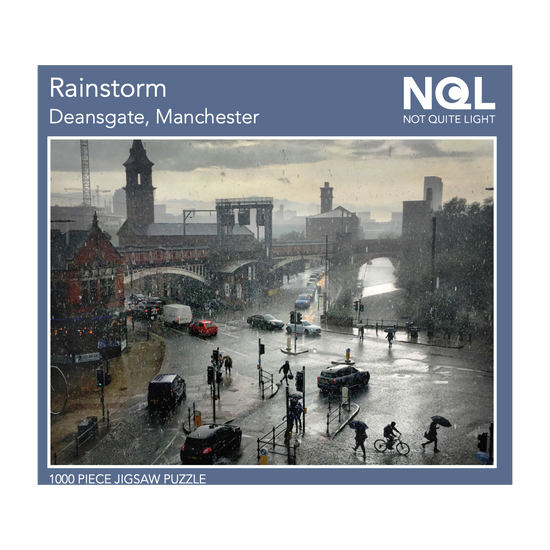 The Not Quite Light rainstorm  jigsaw box seen head on. The image that makes up the jigsaw is surrounded by a dusty blue border and white text with the title and NQL branding.