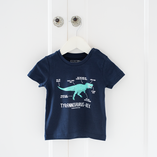 Lifestyle shot of the t. rex baby shirt on a white hanger and hung over a clear doorknob on a white door.
