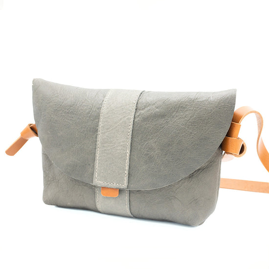 Front view of grey leather bag with tan strap in the background.