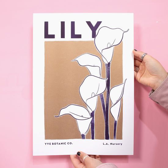 A person holding a print of a lily against pink background