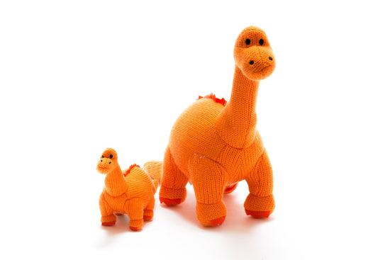 Orange diplodocus knitted plush toy beside the rattle of the same colour.