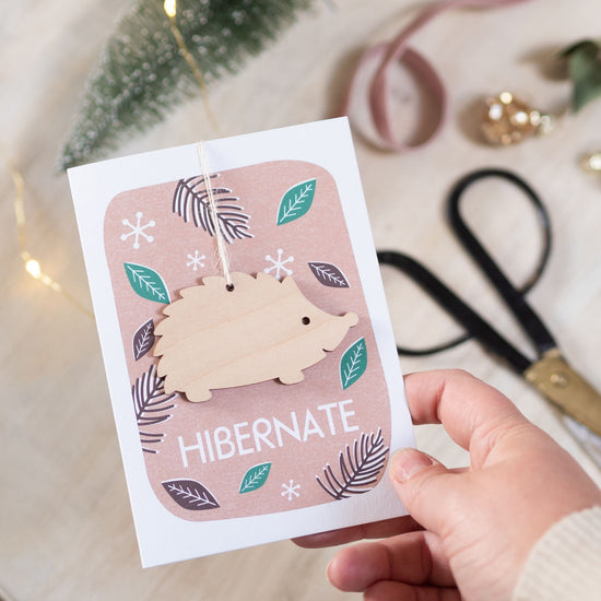 Load image into Gallery viewer, Lifestyle short of hedgehog card with a hand holding the card by the bottom right corner. In the background can be seen a set of scissors and some lights.
