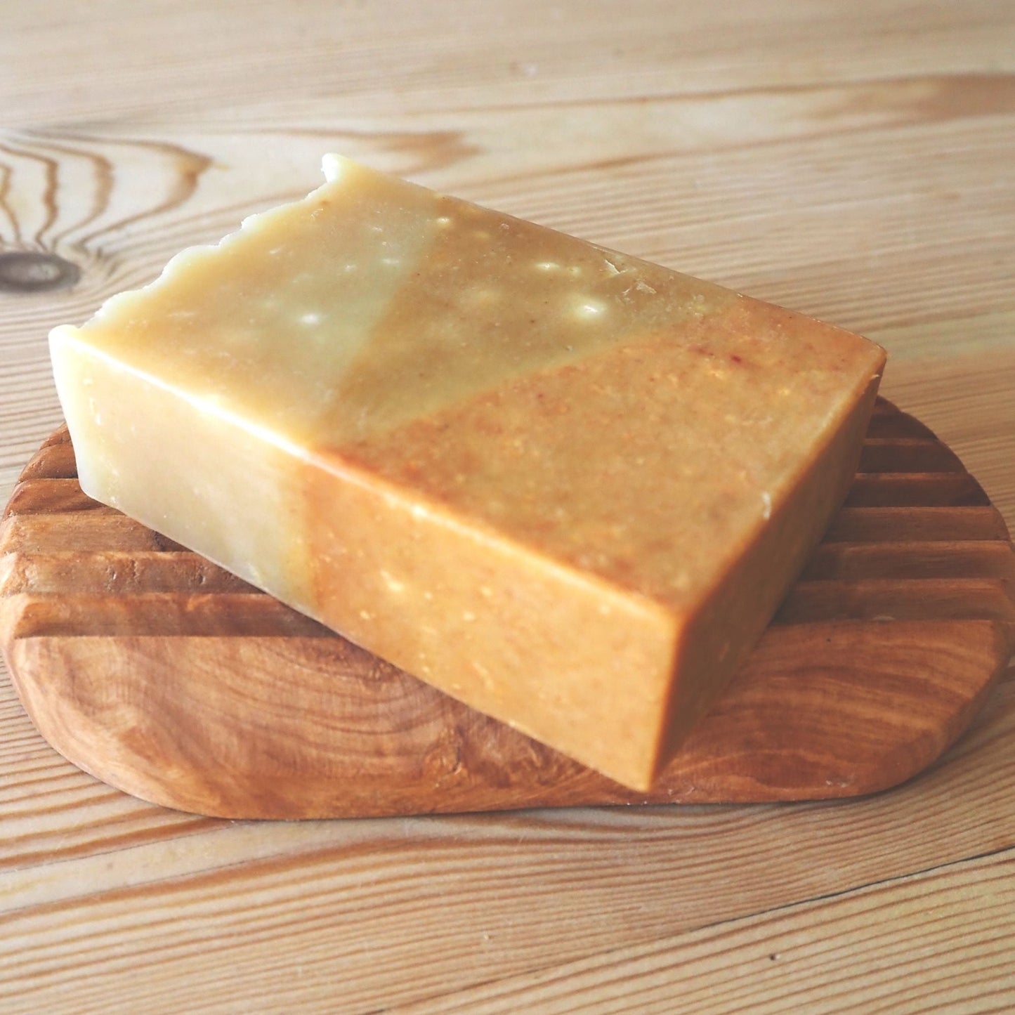 The tricolour soap lying on a wooden soap holder. The soap is orange at the bottom, golden brown middle section and pale golden beige at the top.