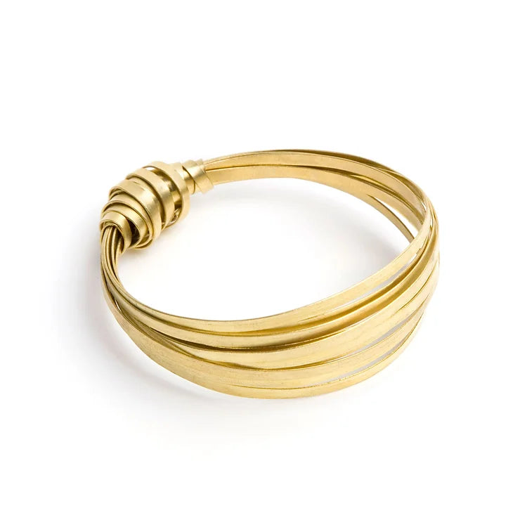 A bangle made with several hoops of brass and with a ribbon knot tied around these hoops on one edge. White backdrop.