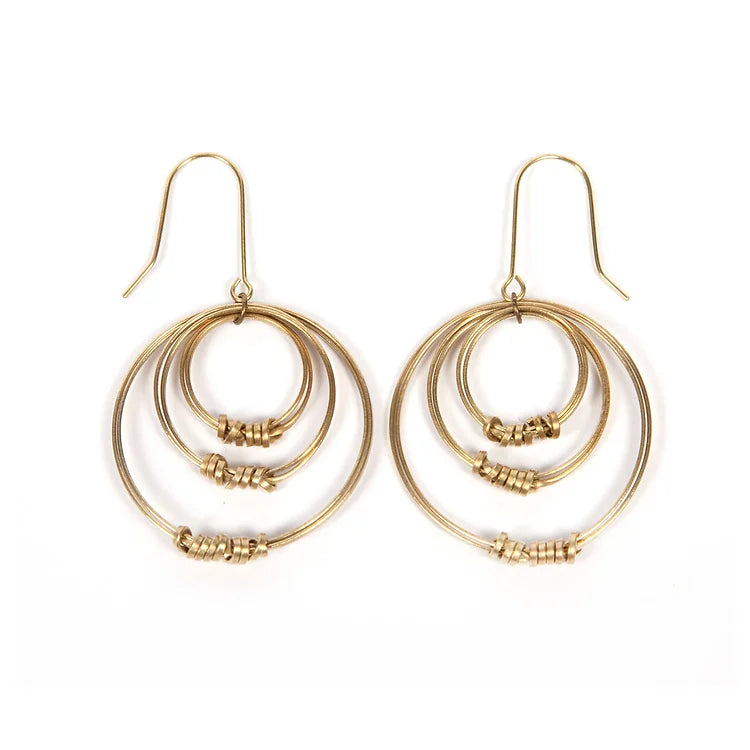 Triple hoop brass earrings seen from the side so all three hoops are clearly visible. The bottom of each hoop has has a brass thread wound around it like a simple ribbon. White backdrop.