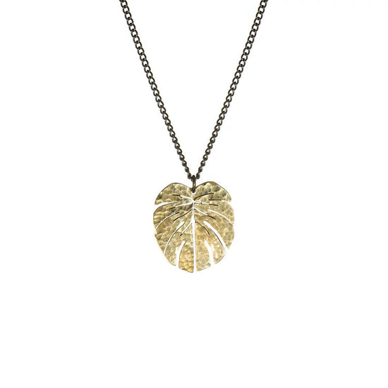 The small brass pendant shaped as a monstera leaf on a white background.