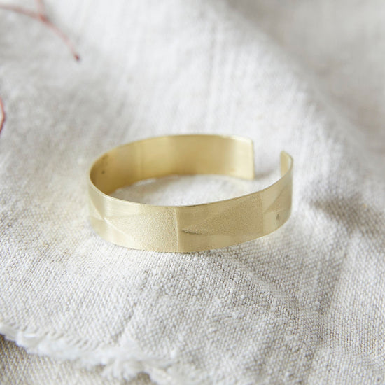 Lifestyle shot of brass bangle with triangular imprint patterns on a natural linen fabric.