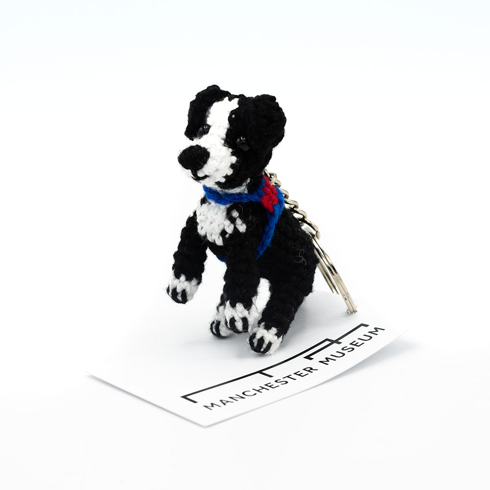 Load image into Gallery viewer, Hand crocheted Murray the therapy dog keyring. Black and white dog sitting on the museum branded white card swing tag.
