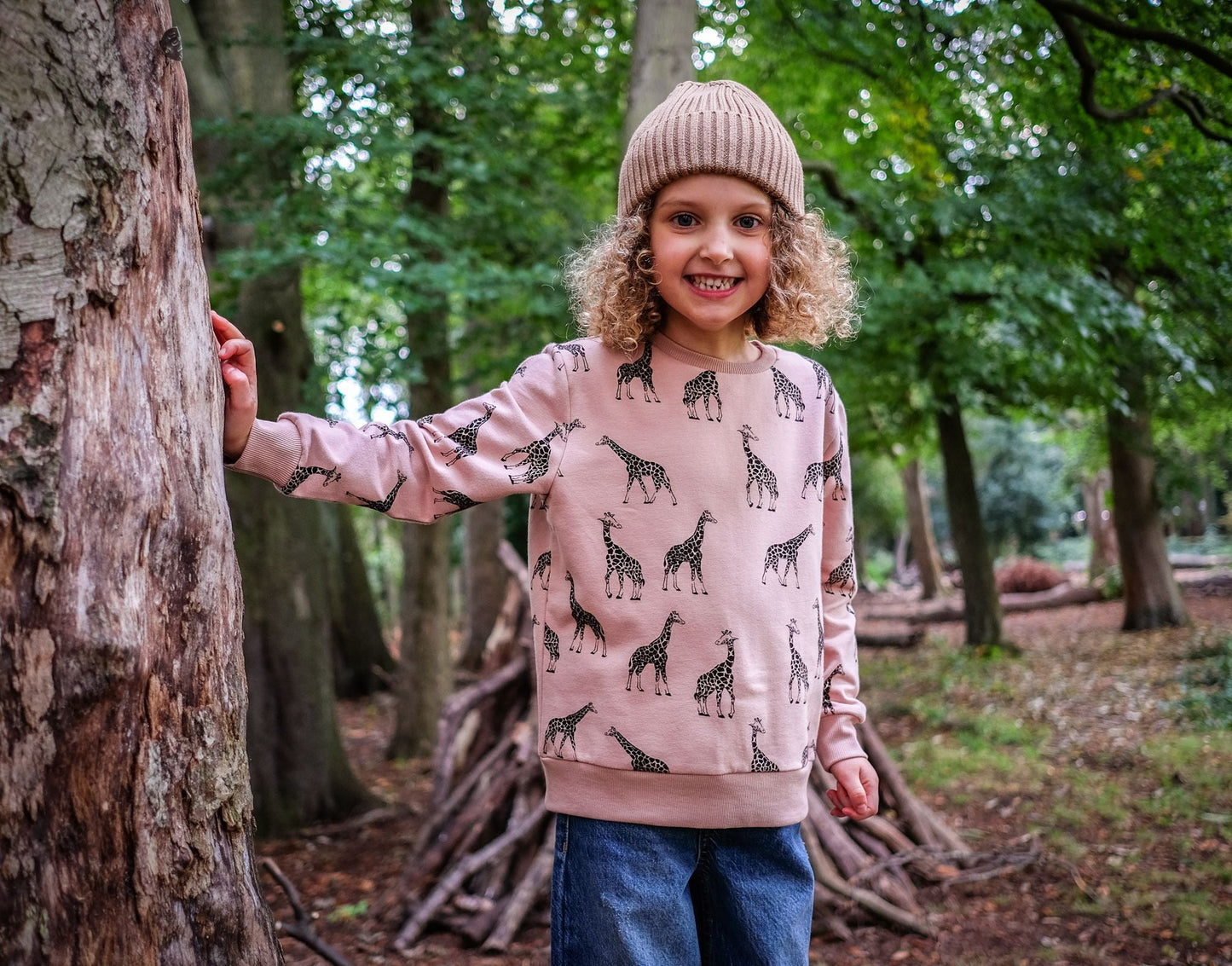 Lifestyle shot of a child wearing the sweatshirt. The background is an open, green woodland.