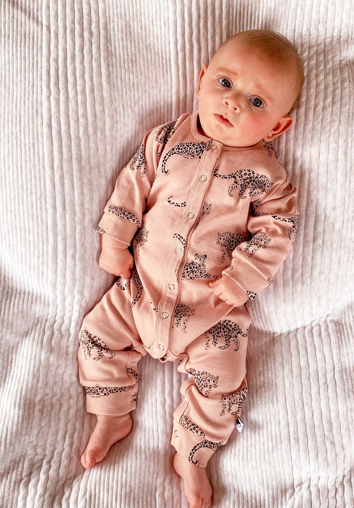 Lifestyle shot of a baby wearing the romper and lying on a white blanket.