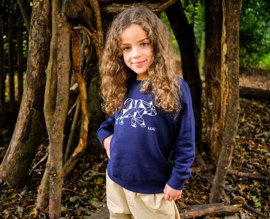 Lifestyle shot of a child wearing the polar bear sweatshirt while standing in front of tree trunks.