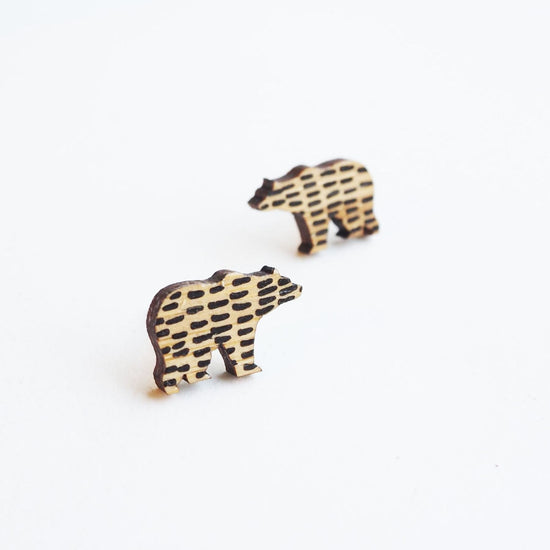 The bear shaped earrings with one in the foreground and the other slightly out of focus. The bamboo can be seen although black horizontal lines dot the bears bodies.