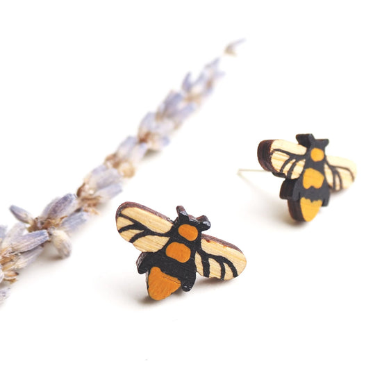 The bee earrings with one in the foreground seen straight on and the other to the right and slightly out of focus. A lavender stalk on the left.