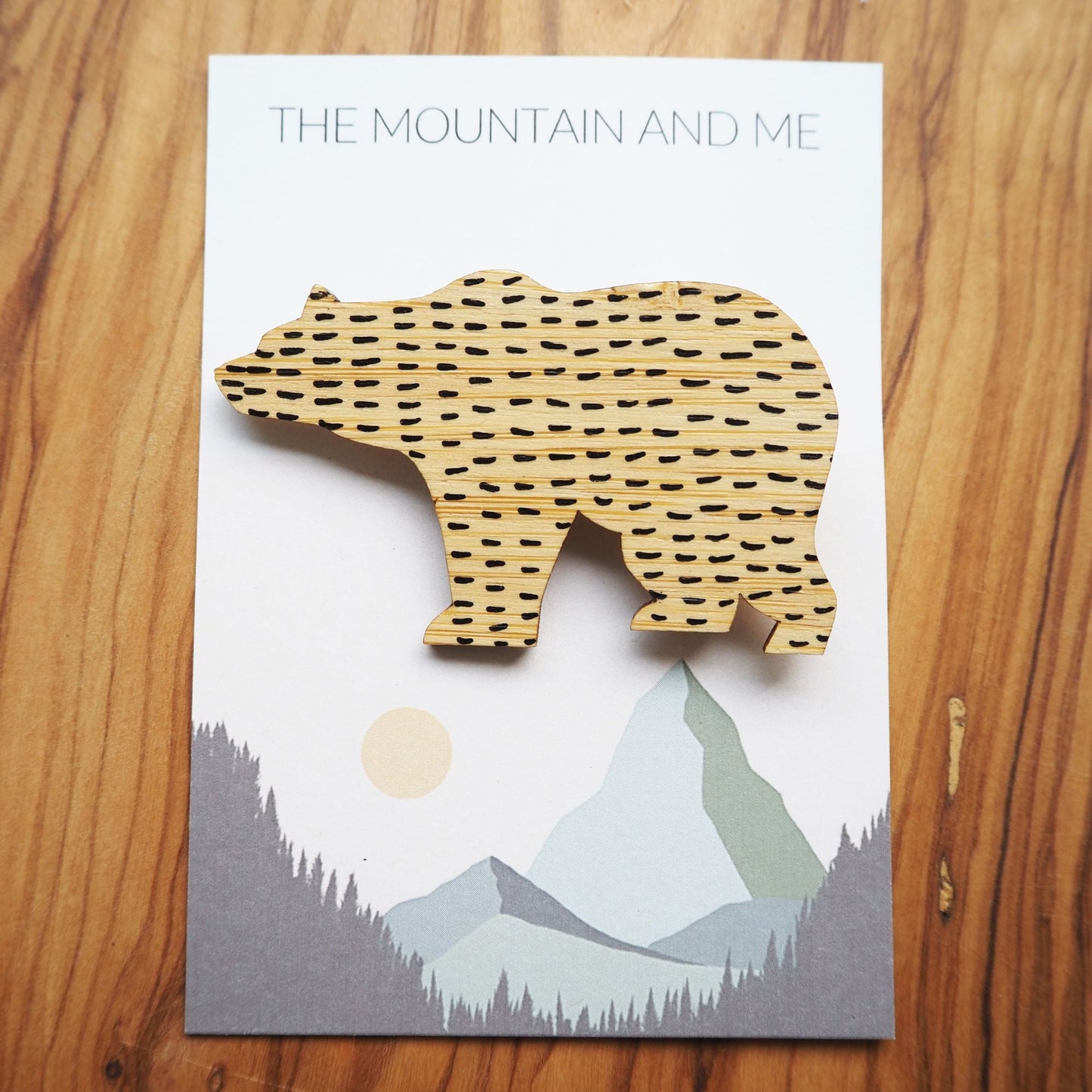 Bamboo bear brooch on the backing card that has The Mountain and Me branding and text. The bear has black short lines in a horizontal pattern all across it.
