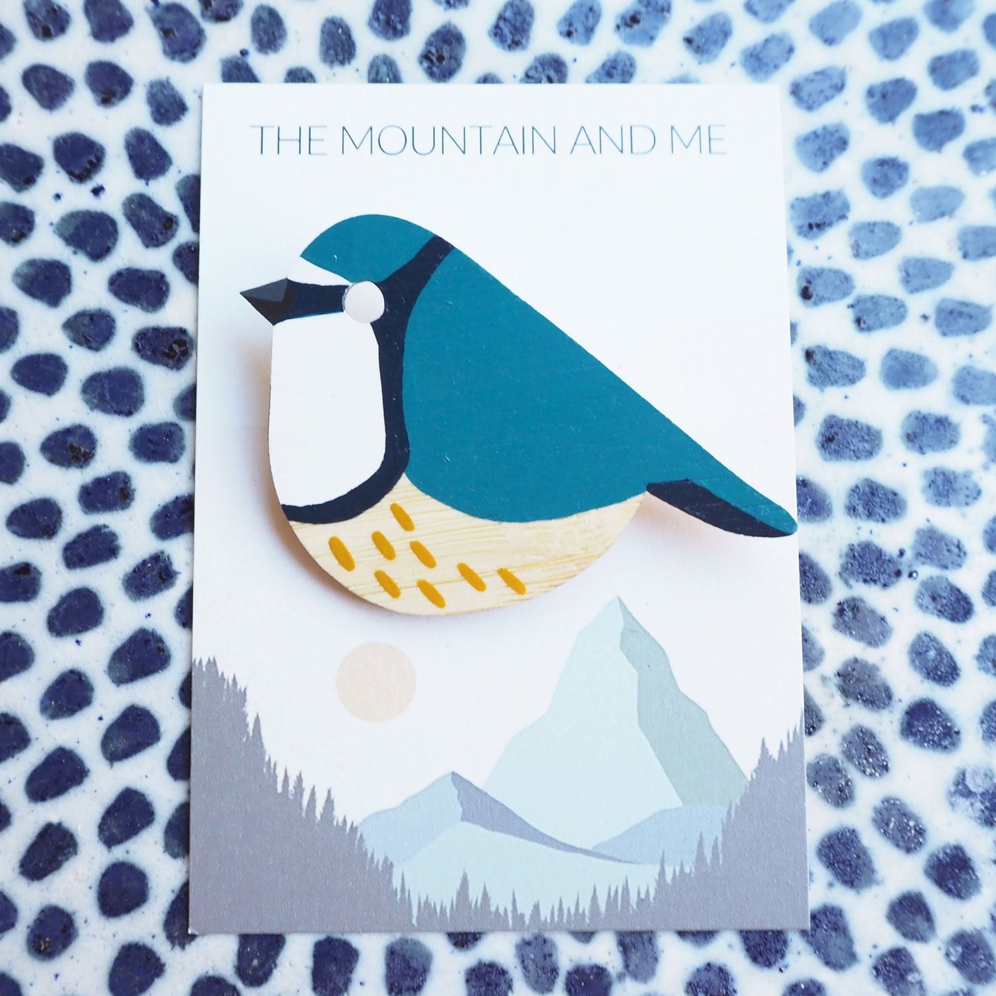 Blue tit bamboo brooch on the Mountain and Me branded backing card. The background is a blue dotted white tile.