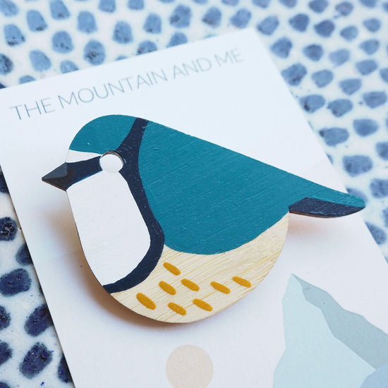 Close up of the blue tit bamboo brooch on the Mountain and Me branded backing card. The background is a blue dotted white tile.