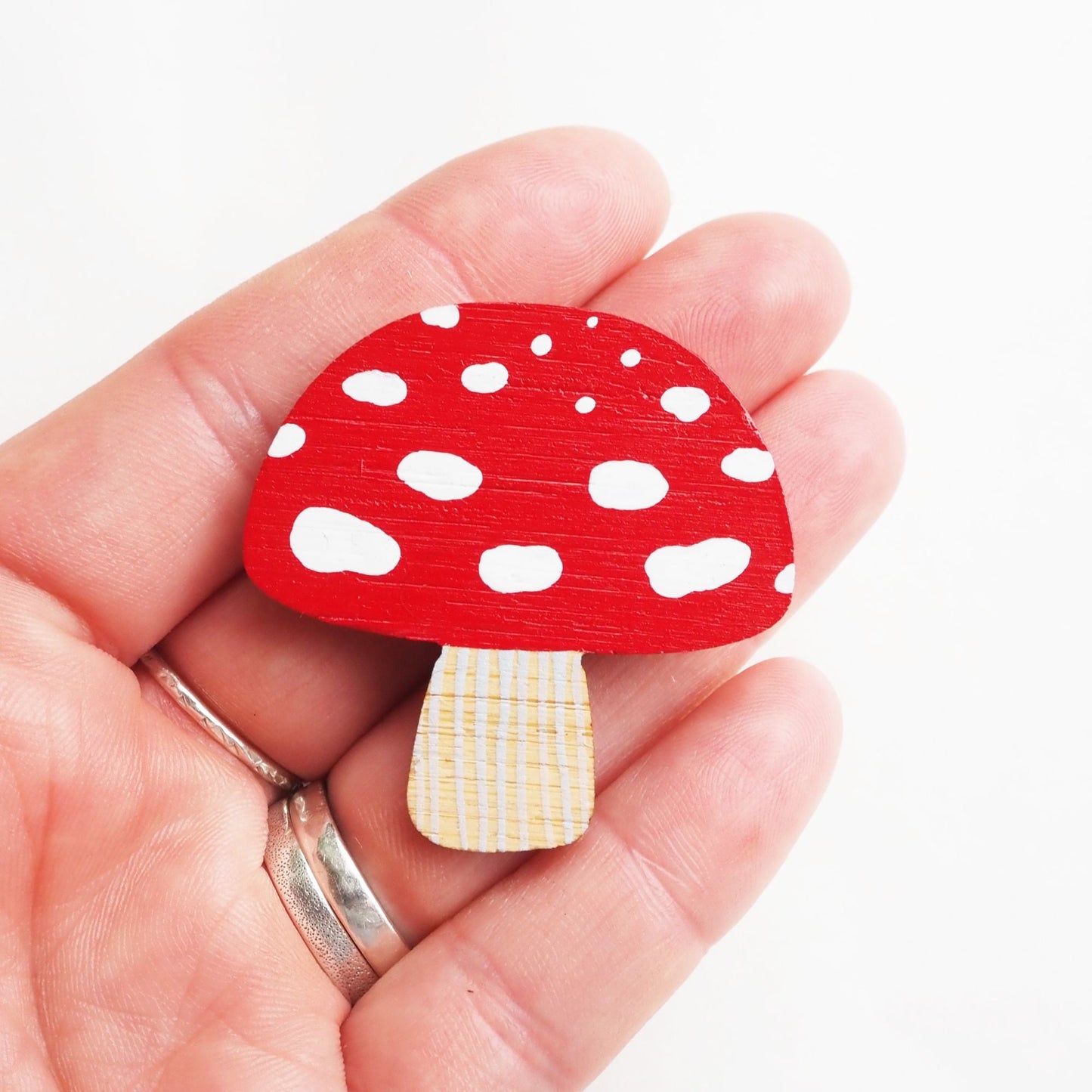A toadstool brooch resting on four fingers. White backdrop.
