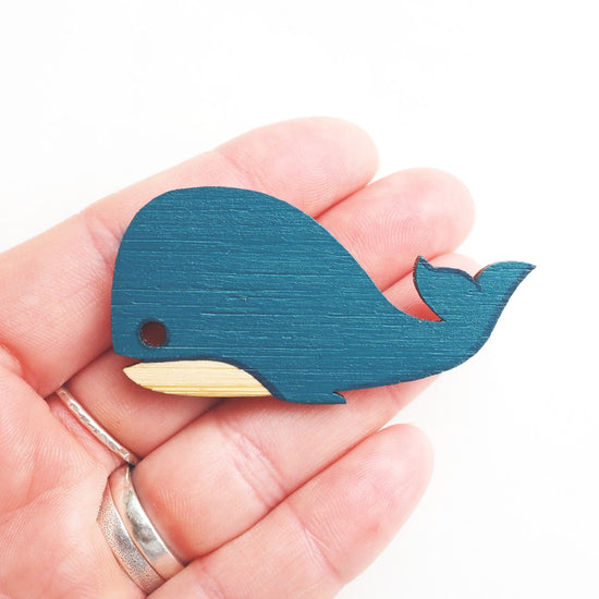 Whale brooch resting on the tip of four fingers. White background.