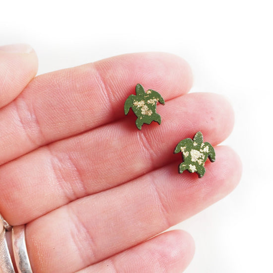 The turtle earrings being held between three fingers.