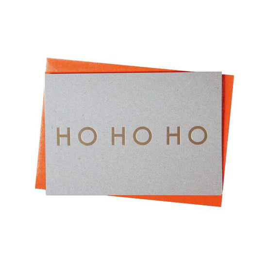 Grey card with brass foil text reading, ho ho ho. Orange envelope in the back.