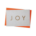 Grey card with brass lettering saying, joy. Orange envelope behind the card.