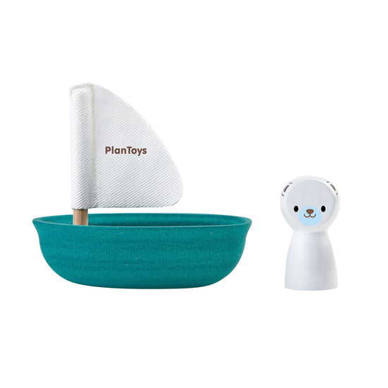 A dark turquoise boat with a white sail and the little polar bear puppet sitting beside it. White backdrop.