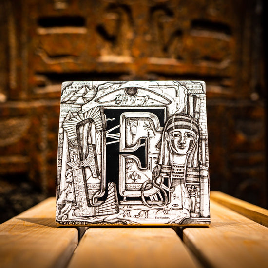Lifestyle shot of the Egypt and Sudan tile by the Sculpts. The tile is standing ona  slatted wooden surface in front of an Egyptian stele with Hieroglyphic carvings on it.