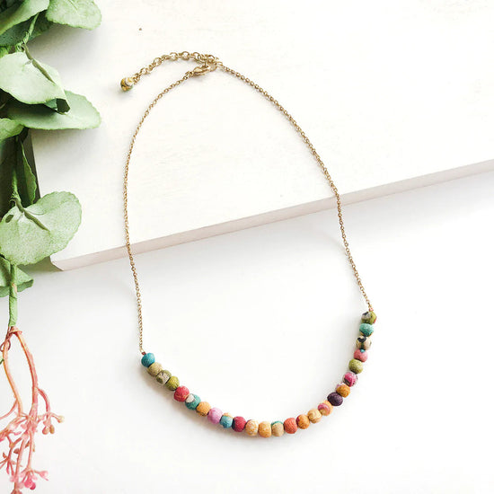 Lifestyle shot of the golden necklace with small kantha beads at the bottom agaisnt a white background.